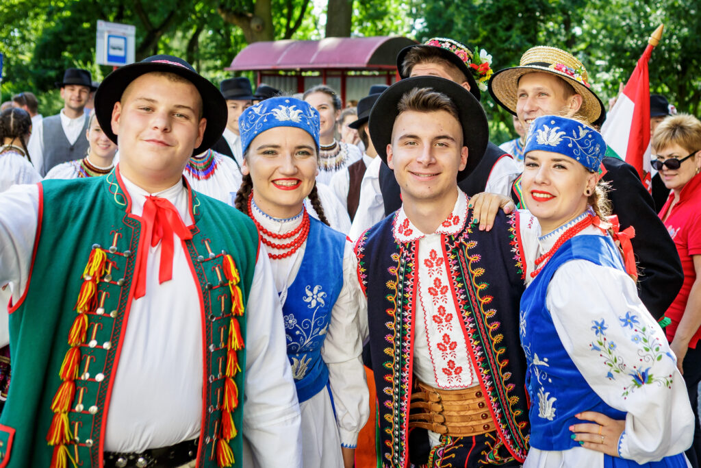 Zdjęcie przedstawia dwie kobiety i dwóch mężczyzn z Zespołu Ludowego Ożarowiacy, ubranych w polskie stroje ludowe, w tle inni członkowie zespołów występujących na Międzynarodowym Festiwalu Folkloru