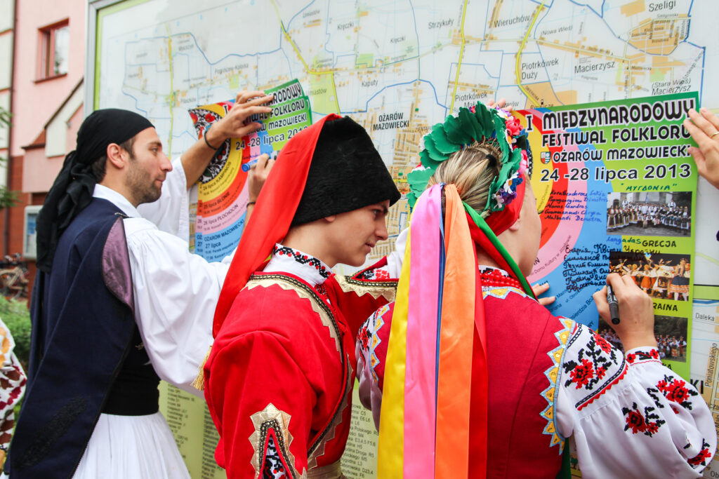 Zdjęcie przedstawia kobietę i dwóch mężczyzn podpisujących się na plakatach Międzynarodowego Festiwalu Folkloru